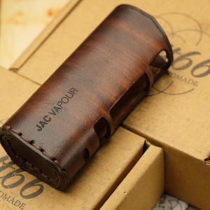 May include: A brown leather case with the text "JAC VAPOUR" embossed on the side. The case is designed to hold a vape device.