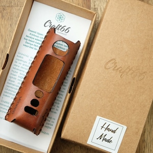 Puede incluir: Una funda de cuero marrón con detalles de costura para un dispositivo electrónico. La funda está en una caja de cartón con las palabras "Craft66" y "Hand Made" impresas en ella.