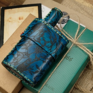Peut inclure: Une flasque en cuir faite à la main avec un motif floral bleu. La flasque est enveloppée dans une sangle en cuir assortie. La flasque est sur une boîte marron, une boîte verte attachée avec de la ficelle et un morceau de toile de jute.