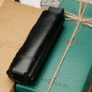 Può includere: Una custodia in pelle nera con la scritta "Craft66" impressa in rilievo. La custodia è appoggiata su una scatola verde con la scritta "Craft66" impressa in rilievo. La scatola è legata con uno spago.