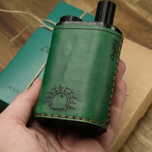 Peut inclure: Un étui en cuir vert avec un dessus noir et une bordure cousue brune. L'étui présente un motif circulaire avec le texte "Firelighter 2" et des chiffres autour du cercle. Le texte "Breath" est gravé sur le côté de l'étui.