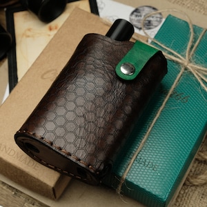 Peut inclure: Une bouteille de voyage en cuir marron avec un motif en nid d'abeille et une sangle en cuir vert. La bouteille est faite à la main et est livrée dans un coffret cadeau vert avec un nœud en ficelle marron.