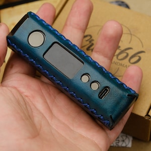 Puede incluir: Una funda de cuero azul verdoso con costuras azules para un dispositivo electrónico. La funda tiene una pequeña pantalla, dos botones y un puerto USB-C.