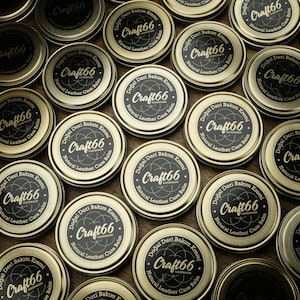 May include: Multiple round containers of natural leather care balm labeled "Craft66 Handmade" with a black and white logo. The containers are gold with black lettering and are arranged on a wooden surface.
