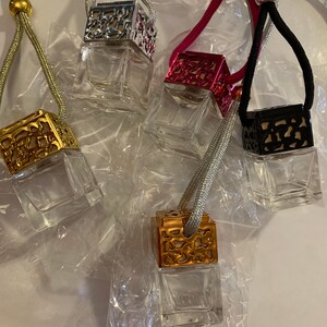 May include: Four glass car air fresheners with decorative metal tops. The tops are silver, gold, pink, and black. Each air freshener is attached to a string.