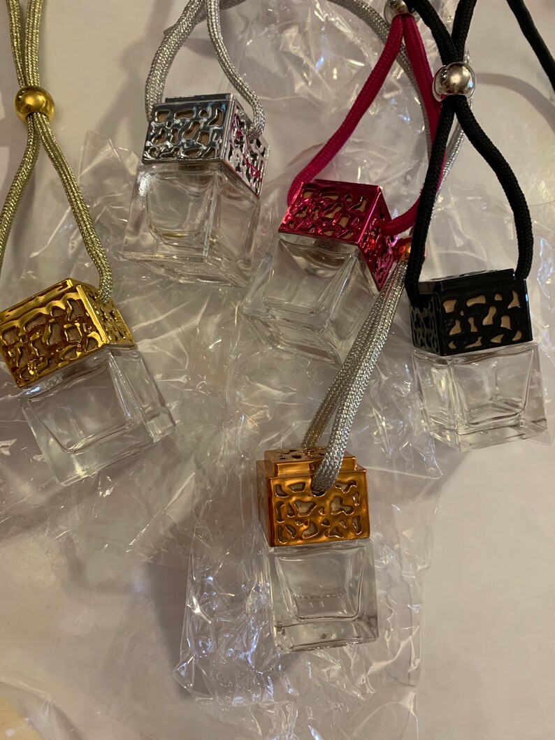 May include: Four glass car air fresheners with decorative metal tops. The tops are silver, gold, pink, and black. Each air freshener is attached to a string.