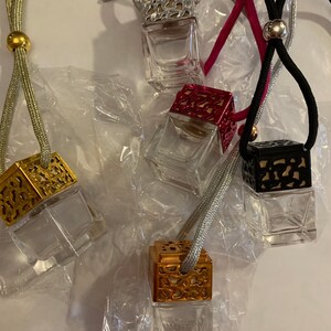 May include: Five decorative car air fresheners with different colored metal caps and clear glass bottles. The air fresheners are hanging from strings with beads.