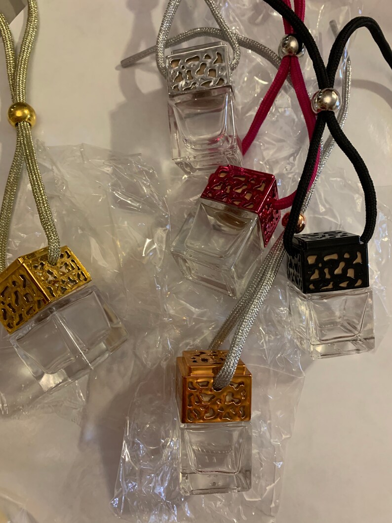 May include: Five decorative car air fresheners with different colored metal caps and clear glass bottles. The air fresheners are hanging from strings with beads.