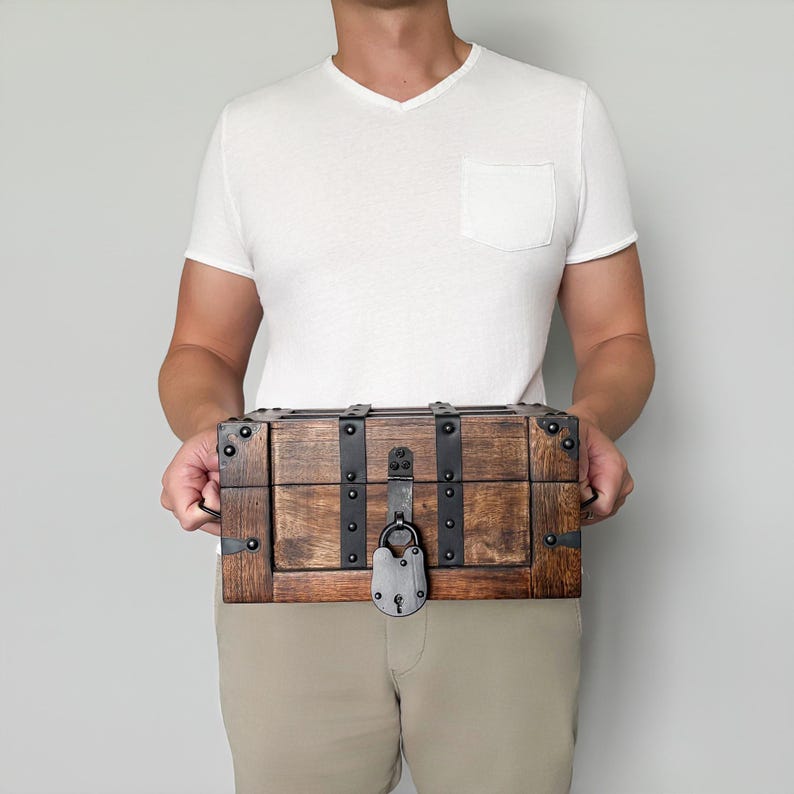 May include: A wooden treasure chest with metal accents and a lock. The chest is rectangular with a dark brown finish and black metal straps and corner pieces. The lock is a silver color.