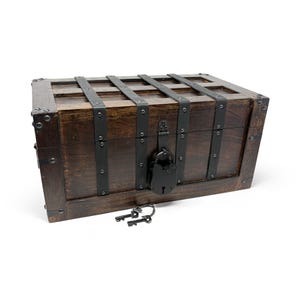 May include: A dark brown wooden chest with metal bands and a black lock. Two keys rest in front of the chest. The chest has a rectangular shape with a hinged lid and is likely used for storage or decoration.