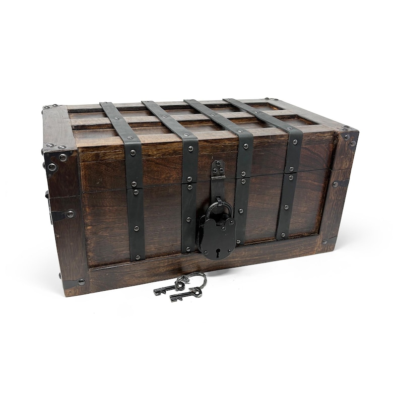 May include: A dark brown wooden chest with metal bands and a black lock. Two keys rest in front of the chest. The chest has a rectangular shape with a hinged lid and is likely used for storage or decoration.
