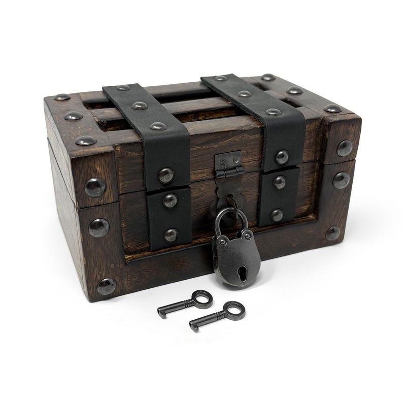May include: A small, rectangular wooden chest with dark brown stain, black leather straps, and metal studs. The chest is secured with a black padlock and comes with two small keys. The overall design evokes a vintage or antique aesthetic.