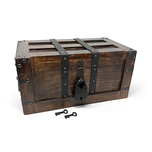 May include: A wooden treasure chest with dark brown stain, metal accents, and a black lock. Two small black keys rest in front of the chest. The chest has metal straps and corner reinforcements.