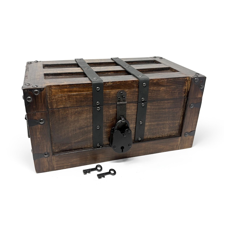 May include: A wooden treasure chest with dark brown stain, metal accents, and a black lock. Two small black keys rest in front of the chest. The chest has metal straps and corner reinforcements.