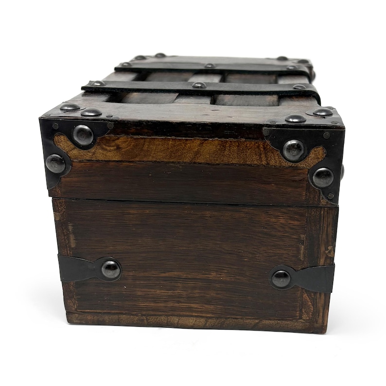 May include: A small, rectangular wooden chest with dark brown stain. The chest features metal bands and corner reinforcements with rivets. The top has a series of horizontal metal bars. The overall design suggests a vintage or antique style.