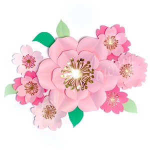 May include: A cluster of pink paper flowers with gold centers. The flowers are arranged in a bouquet-like shape and have a layered, textured appearance.