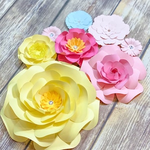 May include: A set of paper flowers in various colors, including yellow, pink, and blue. The flowers are arranged on a wooden surface.