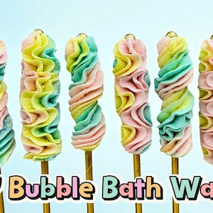 May include: A collection of colourful DIY bubble bath wands on golden sticks. Each wand is a swirl of pastel colours: pink, yellow, and teal. A birthday cake with a lit candle and balloons are in the background.