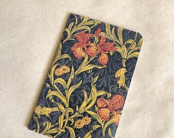 May include: A small notebook with a floral design. The cover features a dark background with yellow, red, and orange flowers and leaves.