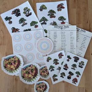 May include: A collection of stickers and cards featuring various designs. Included are cat stickers with floral crowns, bonsai tree illustrations, and circular designs with text. Also present are cards with Shakespearean insults.