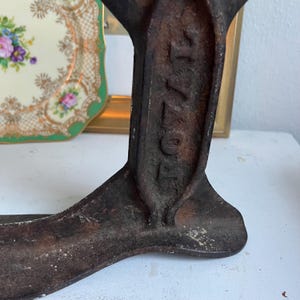 May include: Close-up of a vintage, cast iron shoe last with the word "ROYAL" embossed on the side. The shoe last is dark brown with signs of wear and age. A decorative plate with floral designs is in the background.