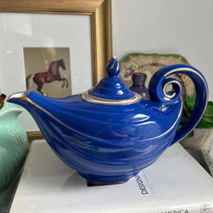 May include: A blue and gold teapot shaped like a genie lamp. The teapot has a swirling design and a gold trim around the lid and spout.