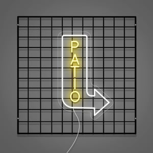 May include: A neon sign with the word "PATIO" in yellow, inside a white arrow-shaped outline. The sign is mounted on a black grid against a gray background. The arrow points to the right.