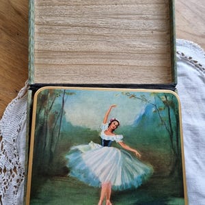 May include: A vintage wooden box with a hinged lid, depicting a ballerina in a white tutu against a forest scene. The box has a green and gold trim and a wooden interior. The ballerina's name is Fontayn.