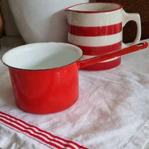 May include: A red enamel saucepan with a white interior and a white and red striped pitcher in the background.