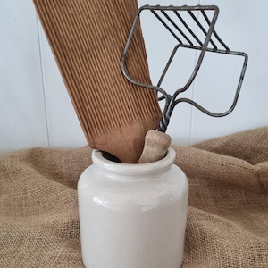 Puede incluir: Un tarro de cerámica blanca con el texto en relieve LAB Lagny que contiene una tabla de madera para ñoquis con estrías verticales y un pasapurés de metal con mango de madera. Los utensilios de cocina están colocados dentro del recipiente.