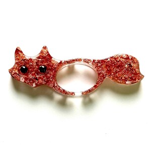 Puede incluir: Un anillo de zorro de color cobre con ojos negros. El anillo está hecho de resina y tiene un acabado brillante.
