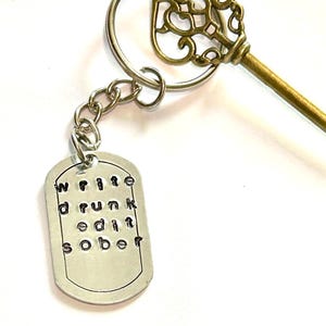 Puede incluir: Un llavero de plata con una llave decorativa y una etiqueta que dice "Escribe borracho edita sobrio".