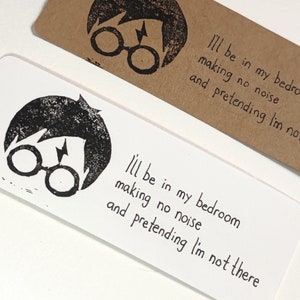 Puede incluir: Dos marcapáginas con temática de Harry Potter con una ilustración en blanco y negro de Harry Potter. El texto en los marcapáginas dice "Estaré en mi habitación haciendo ruido y fingiendo que no estoy ahí."