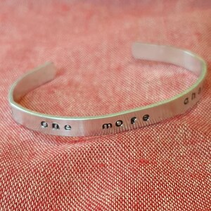 Puede incluir: Pulsera de plata con las palabras "one more" grabadas.