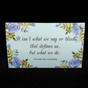 May include: A light blue card with a floral border and a quote from Jane Austen's Sense and Sensibility: "It isn't what we say or think that defines us, but what we do."