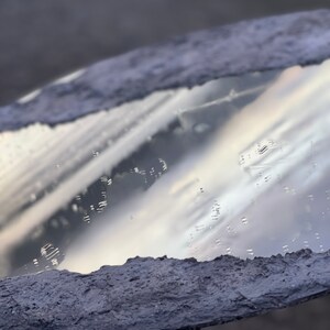 May include: A round mirror with a textured, gray concrete frame. The mirror reflects a cloudy sky.