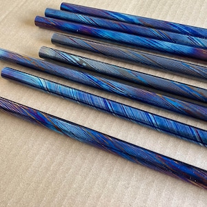 May include: A set of eight blue and gold colored metal rods with a swirling pattern. The rods are arranged in a row on a brown surface.