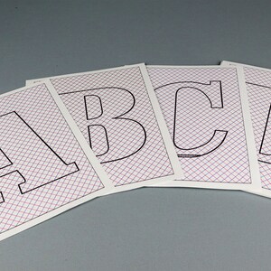 May include: Four white sheets of paper with a grid pattern printed on them. Each sheet has a black outline of a capital letter, A, B, C, and D.