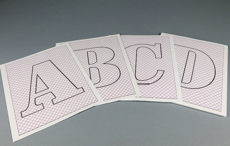 May include: Four white sheets of paper with a grid pattern printed on them. Each sheet has a black outline of a capital letter, A, B, C, and D.