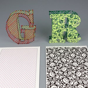 May include: Two letters, "G" and "R", are made of string. The "G" is made with red and yellow string on a grid pattern. The "R" is made with green string on a pattern of circles. Two pieces of paper are below the letters, one with a grid pattern and the other with a pattern of circles.