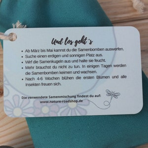 May include: A teal green drawstring bag with a white tag attached. The tag has instructions in German, including sowing instructions for seed bombs. The text includes the website www.nature-roadshop.de.