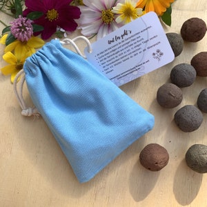 Samenbomben in vier verschieden Sorten, verpackt in einem hellblauen, 100% Baumwollbeutel, daran hängt eine Visitenkarte mit bildlicher und schriftlicher Beschreibung.