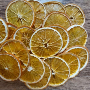 Könnte beinhalten: Ein Stapel getrockneter Orangenscheiben, die in einem Kreis angeordnet sind, auf einer Holzoberfläche. Die Orangenscheiben sind leuchtend gelb-orange und haben ein durchscheinendes Aussehen.