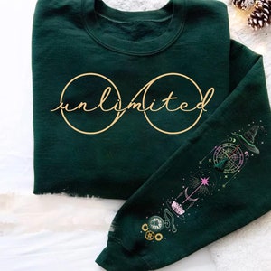 May include: Dark green sweatshirt with the word "unlimited" in gold script and an infinity symbol. The right sleeve features a colorful graphic of a witch's hat, compass, and celestial elements. A cozy and stylish top.