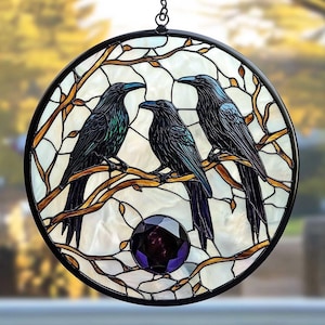 Peut inclure: Un attrape-soleil en verre teinté représentant trois oiseaux noirs perchés sur des branches avec une pierre précieuse violette au centre. Les oiseaux ont des accents bleu et vert irisés.