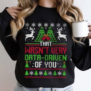 Könnte beinhalten: Schwarzes Sweatshirt mit festlichem Design. Das Design umfasst weiße Rentiere, grüne Weihnachtsbäume, rote Glocken und den Text "THAT WASN'T VERY DATA-DRIVEN OF YOU" in Rot und Grün. Das Sweatshirt hat einen Rundhalsausschnitt.