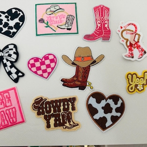 Op de afbeelding: Een verzameling strijklabels met verschillende ontwerpen, waaronder harten, strikken, cowboyhoeden en de woorden "Yee Haw" en "Howdy Y'all".