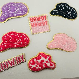 Puede incluir: Un conjunto de 6 parches para planchar con sombreros de vaquero rosas, morados y negros con estrellas blancas y las palabras "Howdy Howdy" en rosa y blanco.