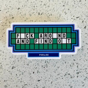 May include: A sticker with a design resembling a game show puzzle board. The phrase "F*CK AROUND AND FIND OUT" is spelled out in white letters on a green background. The word "PHRASE" is written in white on a blue banner.