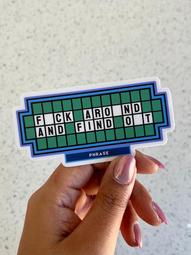 May include: A sticker with a design resembling a game show puzzle board. The text reads "F*CK AROUND AND FIND OUT" in white letters on a green background. The word "PHRASE" is written at the bottom.